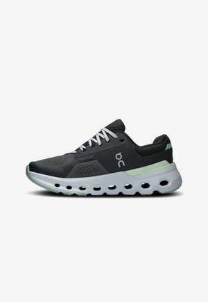 Zapatos deportivos en negro y gris con una parte superior de malla transpirable, cordones blancos y una suela blanca acolchada con acentos verdes y agujeros de ventilación.
