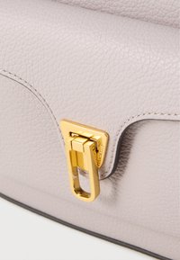 Light lavender leather handbag featuring a textured finish, sleek design, and a gold metal closure with a rectangular loop detail.