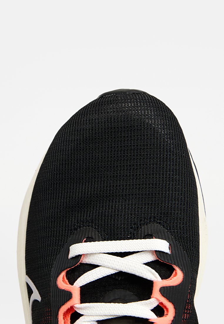 Zapatilla deportiva negra con parte superior de malla, cordones blancos y acentos naranjas. Punta redondeada, suela acolchada y detalles de tela texturizada.