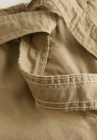 Gros plan sur un tissu beige avec des coutures doubles détaillées et un motif de tissage texturé sur un vêtement.