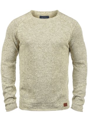 Világos bézs kötött pulóver hosszú ujjakkal, kerek nyakkivágással és textúrázott felülettel. Az alján egy kis barna bőr folt található.