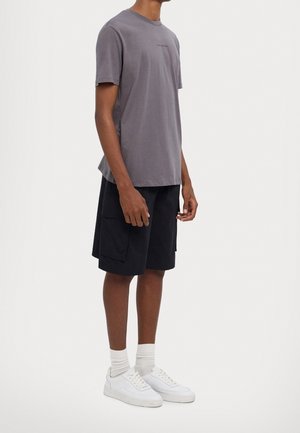 Graues Baumwoll-T-Shirt mit Rundhalsausschnitt, kombiniert mit schwarzen Cargo-Shorts mit mehreren Taschen und weißen Sneakers mit hellgrauen Akzenten.