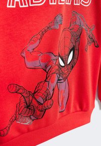 Camiseta roja con un gráfico de Spider-Man en una pose dinámica. El diseño incluye una telaraña negra y rasgos faciales detallados. Textura suave.