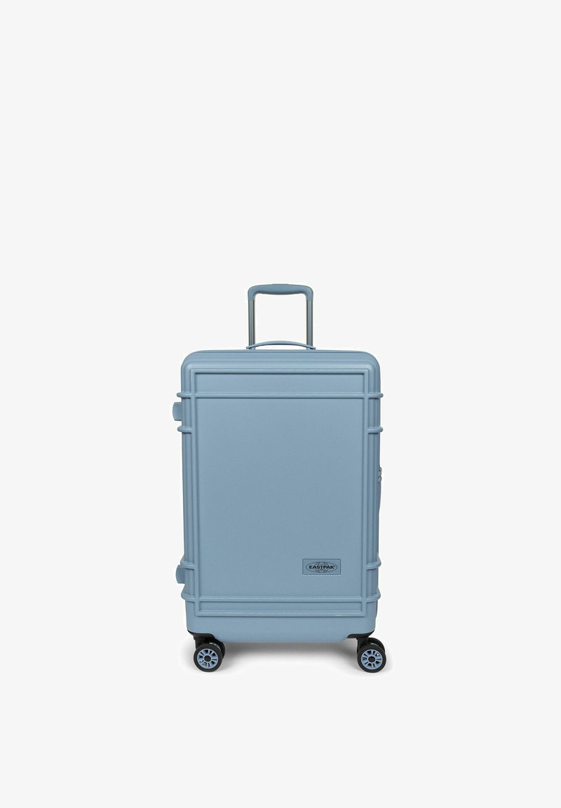 Valise rigide bleu clair avec quatre roues et une poignée rétractable, debout sur un fond blanc.