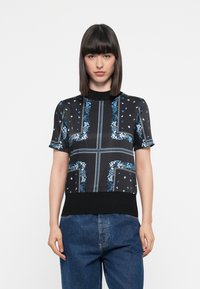Short-sleeved black top with blue floral and geometric patterns, featuring a ribbed neckline and black hem. Smooth, shiny fabric.