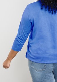 Maglia blu a maniche lunghe con una vestibilità rilassata, caratterizzata da una consistenza morbida, orlo curvo e maniche a tre quarti. Indossata con jeans in denim chiaro.