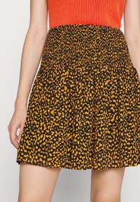 Jupe noire avec imprimé léopard orange, dotée d'une taille smockée et d'une silhouette évasée. Le tissu semble léger et texturé.