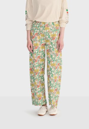 Szerokie spodnie z wysokim stanem w kolorowy kwiatowy i wężowy wzór, noszone z kremową koszulą z długim rękawem i białymi trampkami.