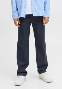 Marineblauwe broeken van een gladde stof, met een rechte pijpzangles. Gecombineerd met witte sneakers voor een casual uitstraling.
