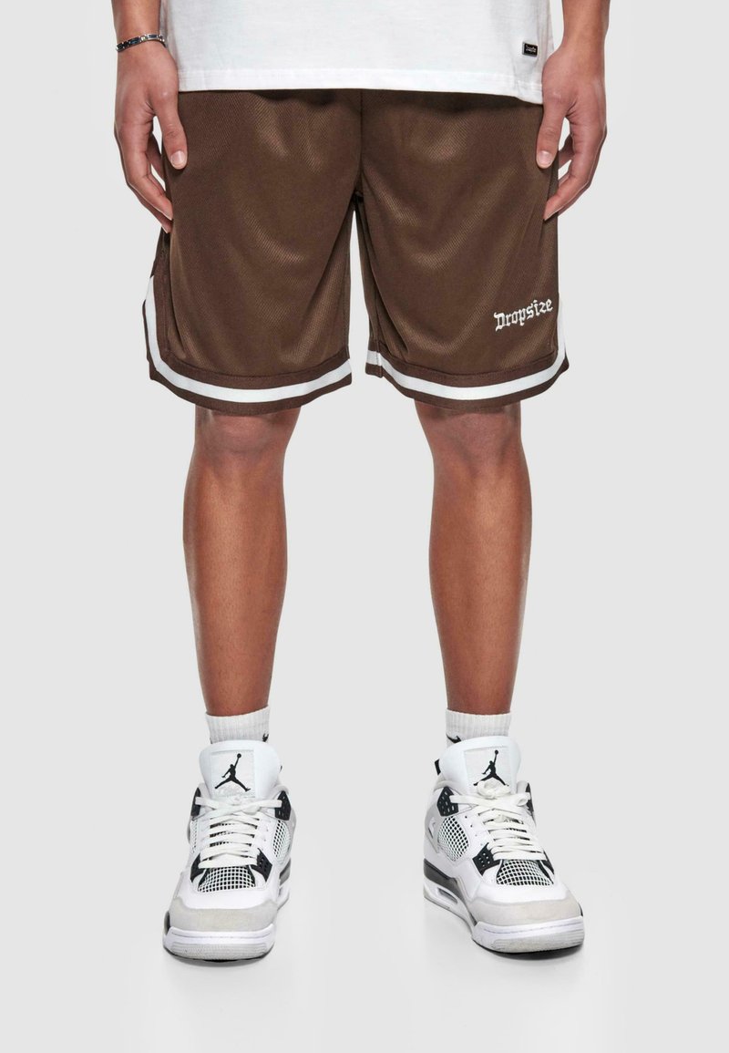Brązowe spodenki sportowe z białymi paskami, wykonane z siateczkowego materiału, z logo "Dropsize" na krawędzi. W połączeniu z białymi i czarnymi sneakersami.