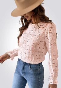 Roze kant blouse met bloemmotieven en lange mouwen. Inclusief gerimpelde manchetten, gecombineerd met lichtblauwe denim jeans.