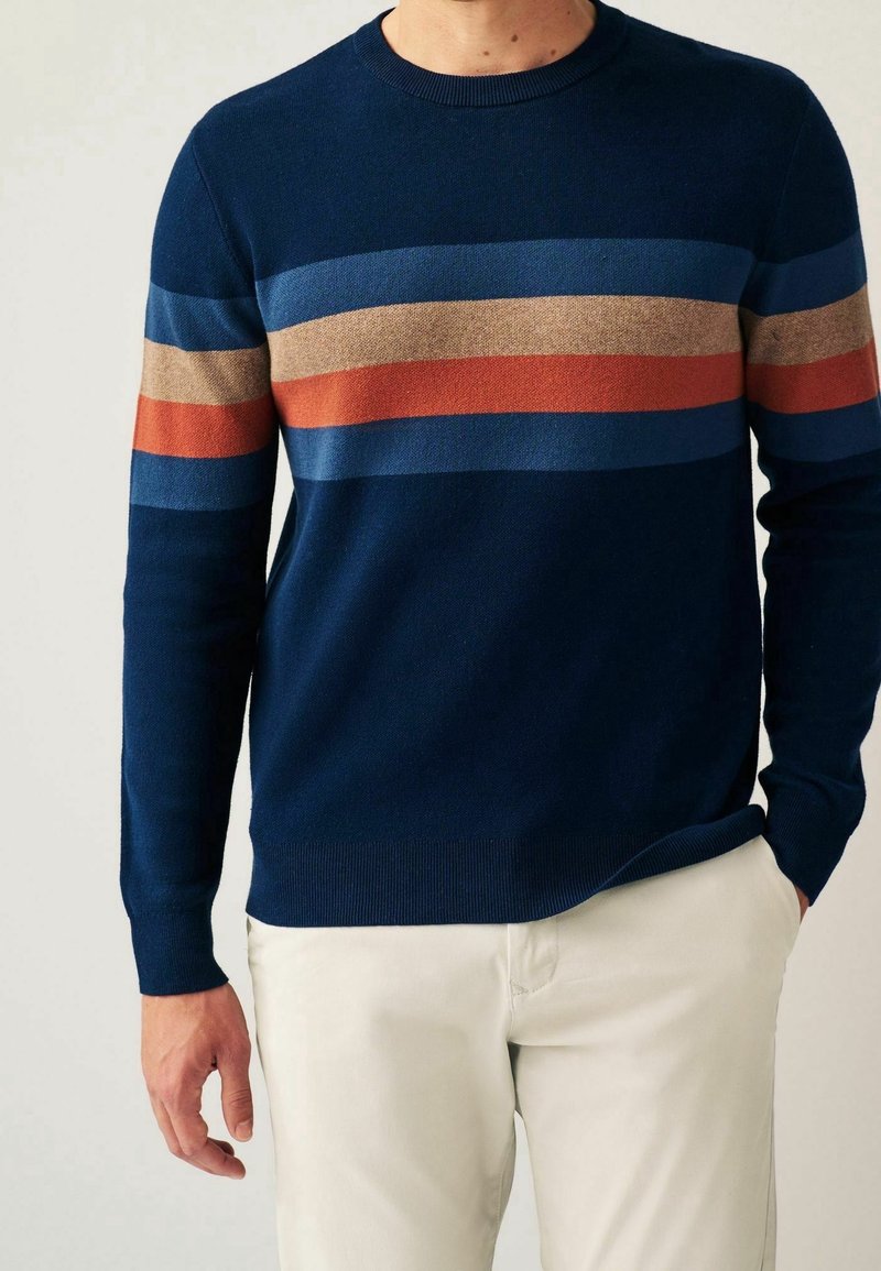 Pull en maille bleu marine avec des rayures horizontales en bleu, marron et rouille. Encolure ronde classique et poignets et ourlet côtelés.