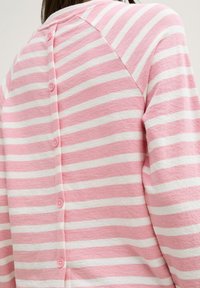 Camiseta de manga larga a rayas rosa y blanca con cuello redondo y cinco botones rosas en la espalda, hecha de una suave tela texturizada.