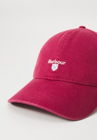 Casquette de baseball en coton rouge avec une visière courbée, arborant un logo "Barbour" brodé et un design de blason à l'avant.