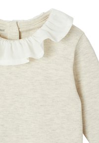 Langärmliges Oberteil aus weichem beigen Stoff, mit einem weißen Rüschensaumkragen und normaler Passform. Die Textur wirkt glatt und leicht.