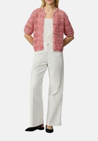 Roze gehaakte cardigan met een ronde hals, korte mouwen en zilveren knopen, gecombineerd met witte wijde broek en zwarte flats.