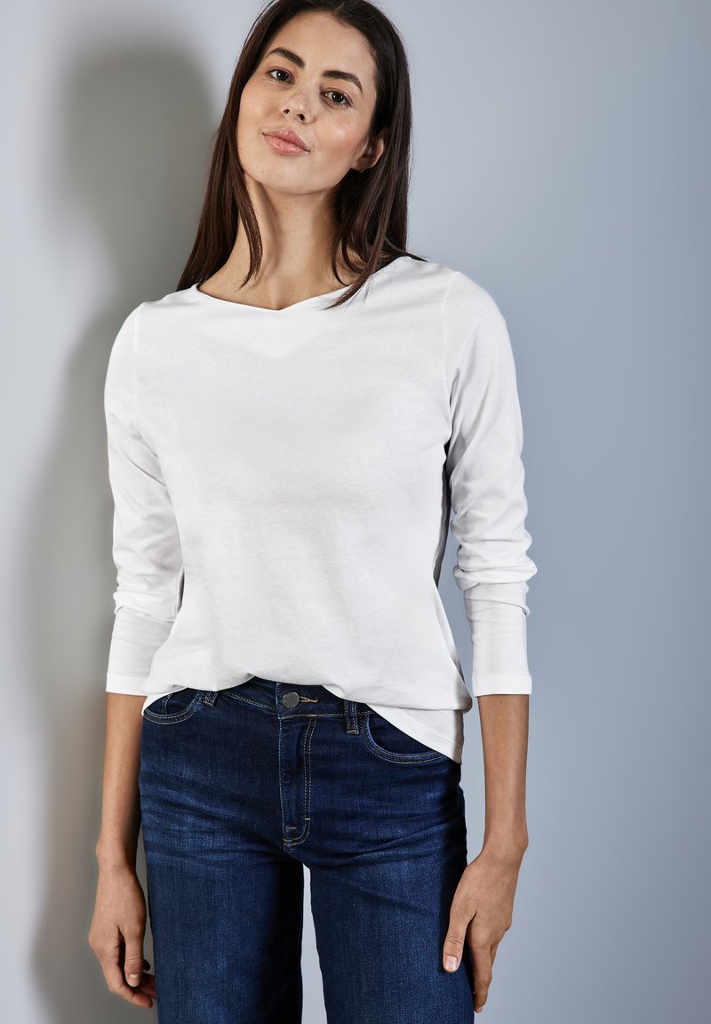Weiße Langarmbluse aus weichem Material mit Rundhalsausschnitt, kombiniert mit dunkelblauen Jeans aus Denim mit normaler Taille und Taschen.