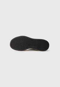 Juodos gumos padas Skechers batų su tekstūruotu sukibimo raštu ant balto fono.