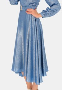 Niebieska metaliczna spódnica z marszczonym elastycznym paskiem i paskiem, z płynnie opadającym asymetrycznym dołem oraz gładką teksturą.