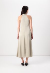 Abito beige con collo all'americana, realizzato in tessuto morbido, che cade a metà polpaccio con una forma svasata. Indossato con scarpe nere con dettagli rotondi.