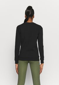 Czarny sweats Hurt z długimi rękawami i ściągaczami, z okrągłym dekoltem i dopasowanym krojem. W połączeniu z zielonymi legginsami w pionowe paski.