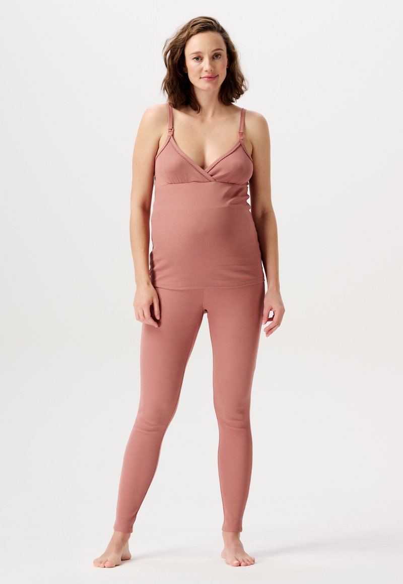 Graviditetsaktivklädesset i mjukt, töjbart, dämpat rosafärgat tyg; inkluderar en åtsittande topp med justerbara axelremmar och matchande leggings.