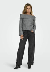 Grauer schulterfreier Pullover mit gerippten Akzenten, kombiniert mit hoch taillierten schwarzen weiten Jeans und schwarzen Stiefeletten mit Absatz.