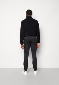 Černá fleecová bunda s vysokým límcem, spárovaná s tmavě šedými cargo kalhotami, které mají boční kapsy a elastické manžety, doplněná bílými teniskami.