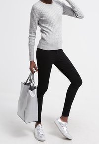 Pull en maille torsadée gris clair, jean noir ajusté, baskets argent métallisé et sac fourre-tout argent texturé avec des accents noirs.
