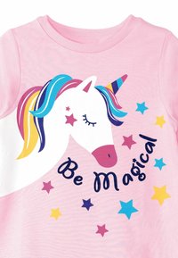 Vaaleanpunainen puuvillapaita, jossa on yksisarvisgrafiikka monivärisine hiuksineen ja sarvineen. Yksisarvisen ympärillä on tähtiä ja teksti "Be Magical" mustalla.