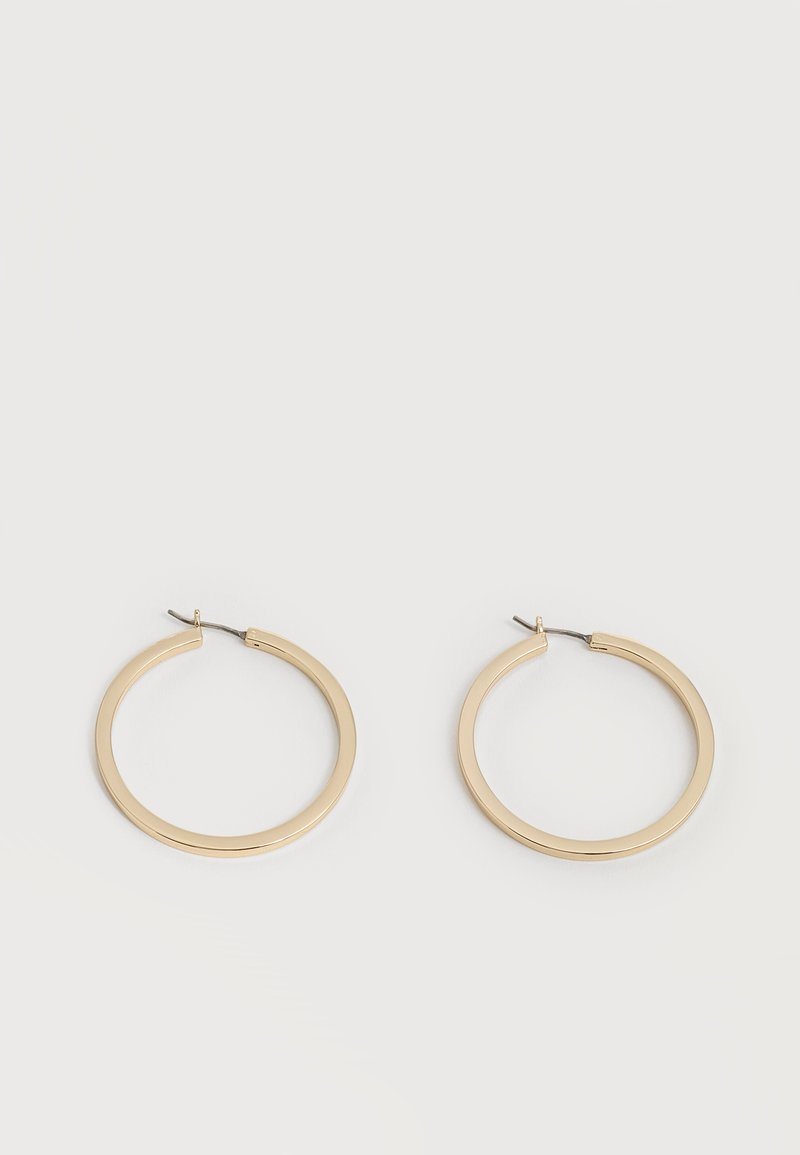Paire de boucles d'oreilles créoles moyennes lisses ton or avec fermoirs à charnière sur fond clair uni.