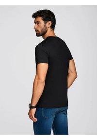 Sort tætsiddende t-shirt med rund hals, korte ærmer og en glat tekstur. Båret med blå jeans, set bagfra.