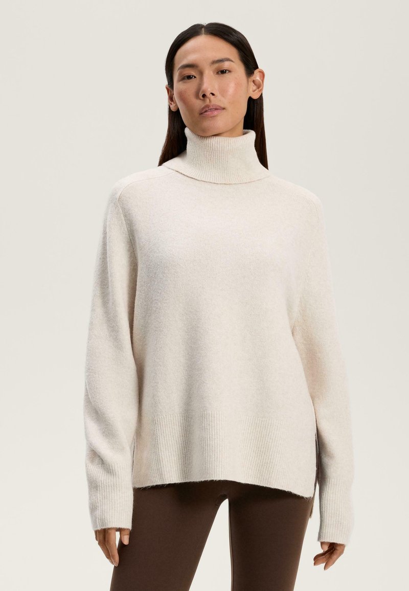 Maglione a collo alto color crema con vestibilità ampia, tessuto testurizzato, polsini e orlo a coste, con una fessura laterale per facilitare i movimenti.