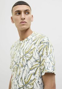 Tricou alb cu guler rotund, având un imprimeu botanic galben și gri, mâneci scurte și o textură moale. Detaliat cu un design lejer.