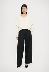 Pull crème oversized avec un design superposé, associé à un pantalon large noir taille haute et des escarpins noirs à bout pointu.