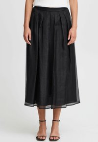 Gonna nera plissettata realizzata in tessuto trasparente, lunga fino al ginocchio con vita aderente. Presenta una texture liscia e un design a strati.