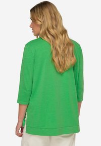 Grünes, locker sitzendes Oberteil mit Dreiviertelärmeln und rundem Ausschnitt. Verfügt über seitliche Schlitze und einen weichen, strukturierten Stoff.