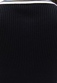 Svart ribbat tyg med en texturerad yta, med en vit och marinblå randig halsringning. Figurnära design med stretch.