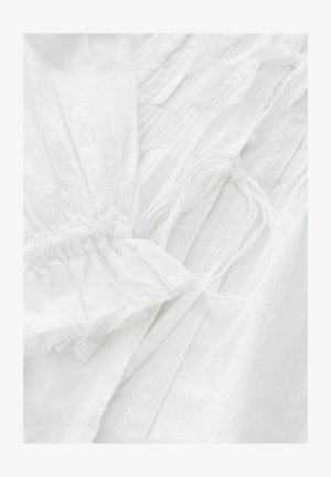 White garment featuring gathered cuffs and ties, with textured and smooth fabric sections, showcasing a blend of patterns and soft finishes.