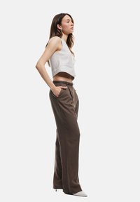 Geknipte lichtgrijze tanktop met verticale strepen, gecombineerd met hoge bruine broek en puntige witte hakken met een textuurpatroon.