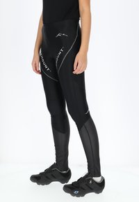 Black cycling tights with a sleek design, featuring a high waist, mesh accents, and reflective detailing. Worn with black cycling shoes.
