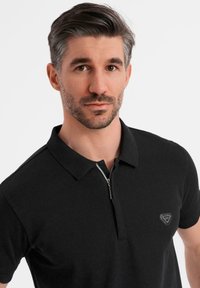 Černé polo tričko z hladké bavlněné směsi se zipovým límcem, s malým trojúhelníkovým logem na levé hrudi.