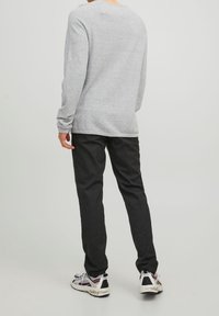 Chemise gris clair à manches longues avec un col rond, associée à un pantalon noir et des baskets multicolores, vue de dos.