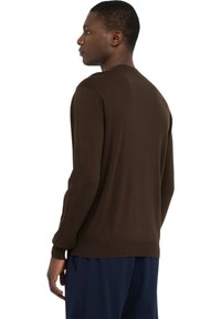 Bruine trui met ronde hals, geribbelde manchetten en zoom, gemaakt van zachte gebreide stof, gedragen over een marineblauwe broek. Zijaanzicht.