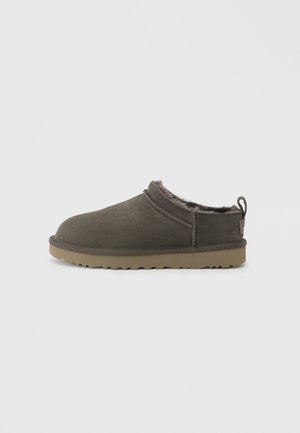 Zapatilla deslizable gris oscuro con forro interior peludo y suela de goma color beige, diseñada para la comodidad y el calor en interiores.