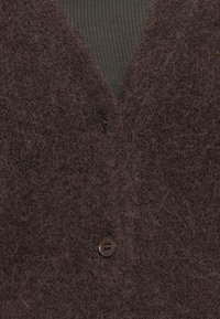 Brązowy puszysty kardigan z dwoma ciemnymi guzikami na żeberkowej oliwkowej koszulce.