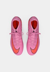 Roze voetbalschoenen met een gestructureerde synthetische bovenkant, contrasterende oranje swoosh, zwarte accenten en platte veters, van bovenaf bekeken.