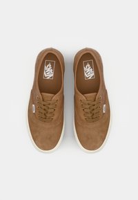 Bruine suède sneakers met beige rubberen zolen, voorzien van vijf oogjes en een wit logo op de tong. Glad oppervlak en klassiek low-top ontwerp.