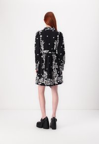 Μαύρο φόρεμα με λευκά λουλουδάτα μοτίβα, μακριά μανίκια και εφαρμοστή μέση. Η φούστα είναι ελαφρώς πλυμένη και συνδυάζεται με μαύρες πλατφόρμες.