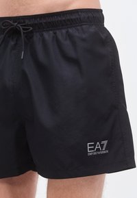 Juodos plaukimo šortai su elastiniu liemeniu, raišteliu ir šoniniu logotipu „EA7 Emporio Armani“ pilka spalva. Lygus, lengvas audinys.